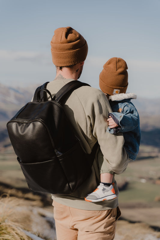 Parent using Oi Oi black dimple faux leather nappy bag backpack on an outdoor family adventure - back